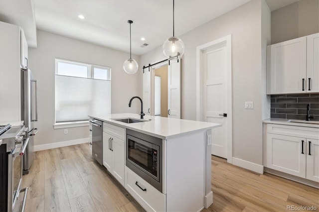 kitchen with sink, appliances with stainless steel finishes, a barn door, a kitchen island with sink, and white cabinets