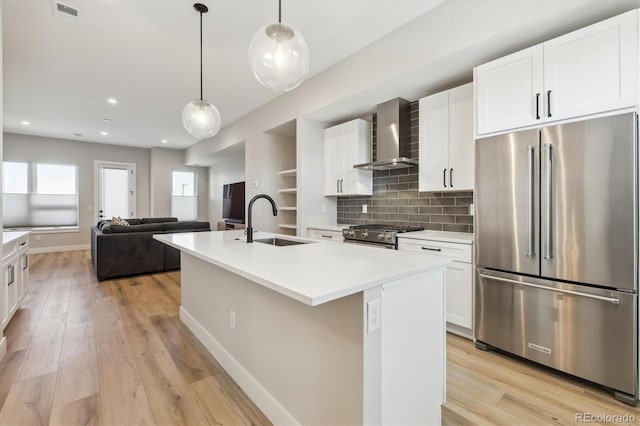 kitchen featuring pendant lighting, sink, premium appliances, a center island with sink, and wall chimney exhaust hood