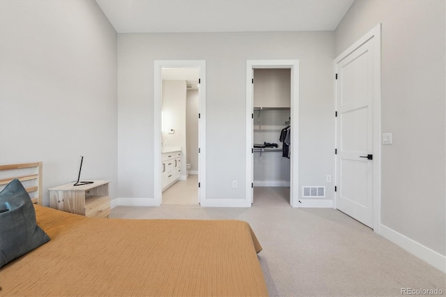 bedroom with a walk in closet, light colored carpet, ensuite bath, and a closet