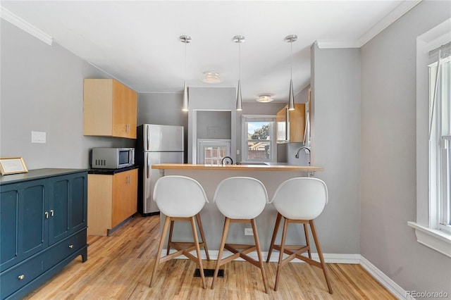 kitchen featuring stainless steel fridge, light wood-type flooring, ornamental molding, decorative light fixtures, and kitchen peninsula