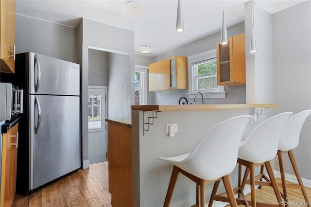 kitchen with a kitchen bar, kitchen peninsula, stainless steel fridge, and light hardwood / wood-style flooring