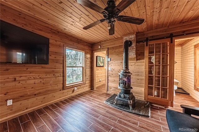 interior space featuring wooden ceiling, a barn door, wood-type flooring, wood walls, and ceiling fan