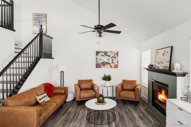 living area featuring dark wood-style floors, stairs, a ceiling fan, and a tile fireplace