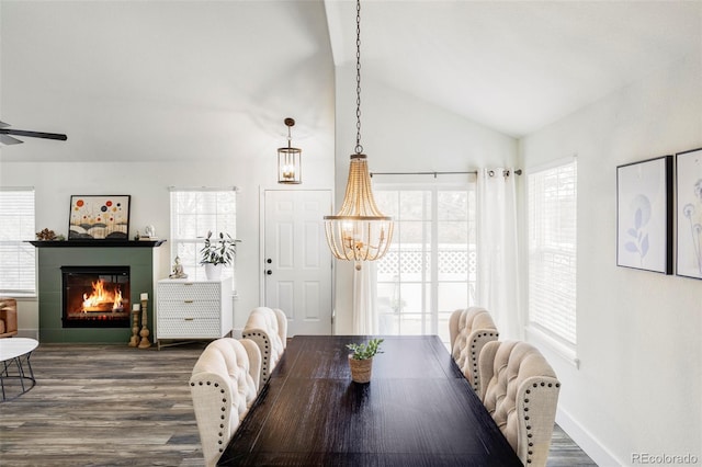 dining space with vaulted ceiling, a glass covered fireplace, wood finished floors, and a healthy amount of sunlight