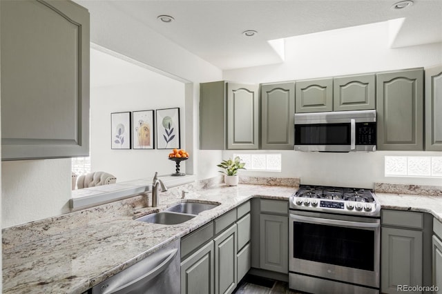 kitchen with light stone counters, stainless steel appliances, gray cabinetry, a sink, and recessed lighting