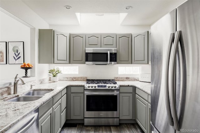 kitchen with dark wood finished floors, light stone countertops, gray cabinets, stainless steel appliances, and a sink