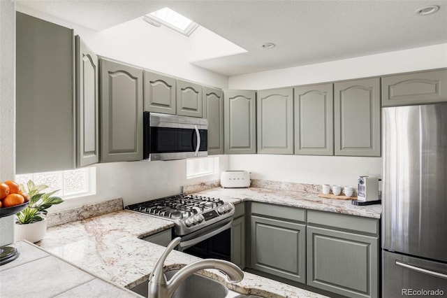 kitchen featuring stainless steel appliances, a skylight, gray cabinets, and light countertops