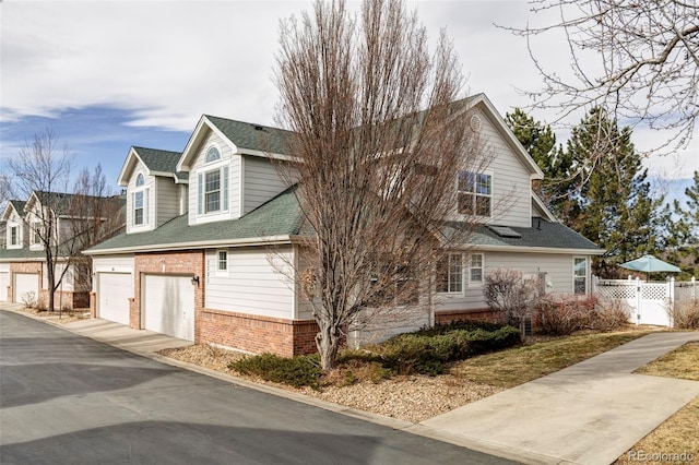 view of home's exterior with a garage, driveway, roof with shingles, fence, and brick siding