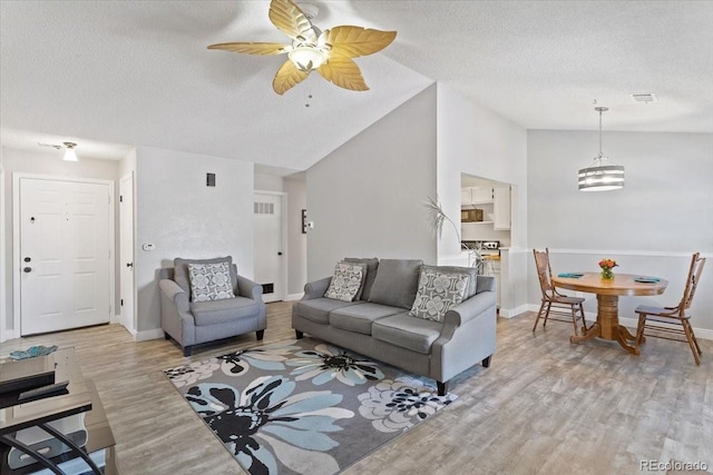 living room featuring lofted ceiling, light wood-type flooring, a textured ceiling, ceiling fan, and baseboards