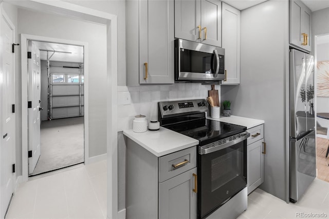 kitchen featuring gray cabinetry, stainless steel appliances, light tile patterned flooring, and backsplash