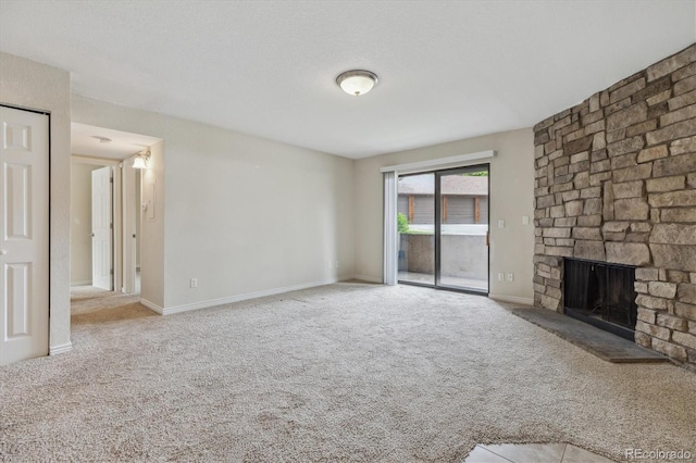 unfurnished living room with carpet, a stone fireplace, and baseboards