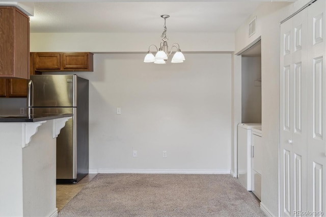 kitchen featuring freestanding refrigerator, a chandelier, washer and clothes dryer, brown cabinets, and light colored carpet