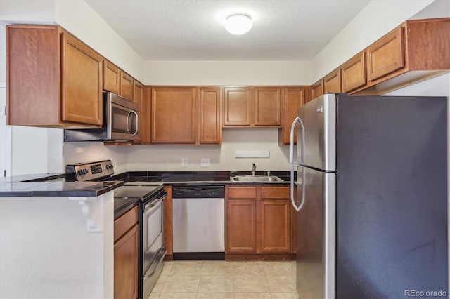 kitchen featuring appliances with stainless steel finishes, dark countertops, a sink, brown cabinets, and a textured ceiling