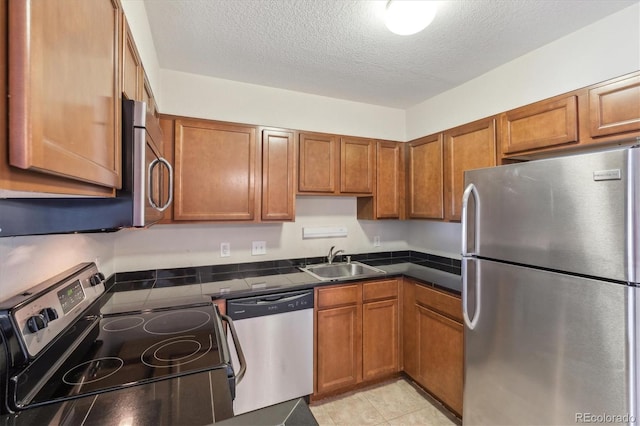 kitchen featuring appliances with stainless steel finishes, a sink, brown cabinetry, dark countertops, and a textured ceiling