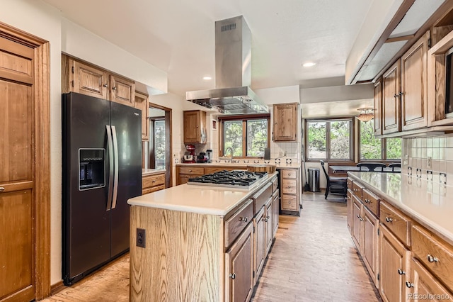 6663 S Prescott Way, Littleton, CO 80120 - kitchen featuring black refrigerator with ice dispenser, island exhaust hood, stainless steel gas stovetop, decorative backsplash, and light countertops