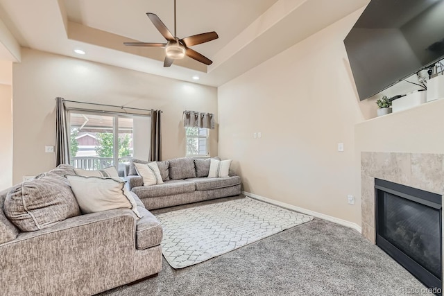 living room with a towering ceiling, carpet floors, a tile fireplace, and ceiling fan