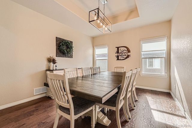 dining area with a raised ceiling and dark hardwood / wood-style flooring