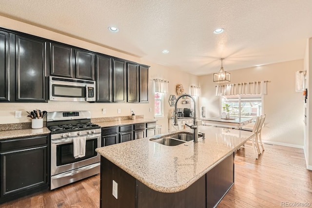 kitchen with hardwood / wood-style flooring, hanging light fixtures, a center island with sink, sink, and appliances with stainless steel finishes