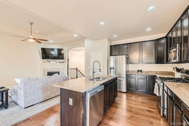 kitchen with an island with sink, stainless steel appliances, sink, light stone counters, and light hardwood / wood-style floors