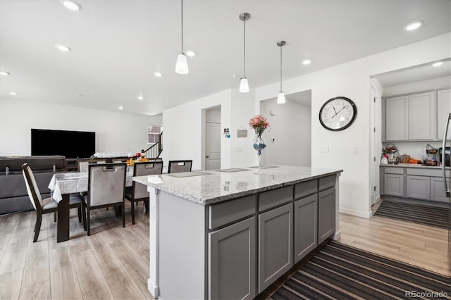 10983 Uvalda St, Commerce City, CO 80022 - kitchen featuring gray cabinets, light wood-style flooring, light stone countertops, a kitchen island, and recessed lighting