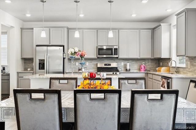 10983 Uvalda St, Commerce City, CO 80022 - kitchen featuring appliances with stainless steel finishes, a sink, a kitchen island, gray cabinets, and tasteful backsplash