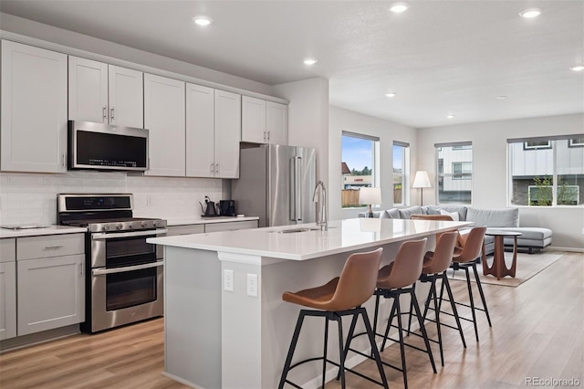 12283 W 57th Ln, Arvada, CO 80002 - kitchen with stainless steel appliances, open floor plan, light wood-type flooring, a kitchen island with sink, and a kitchen bar
