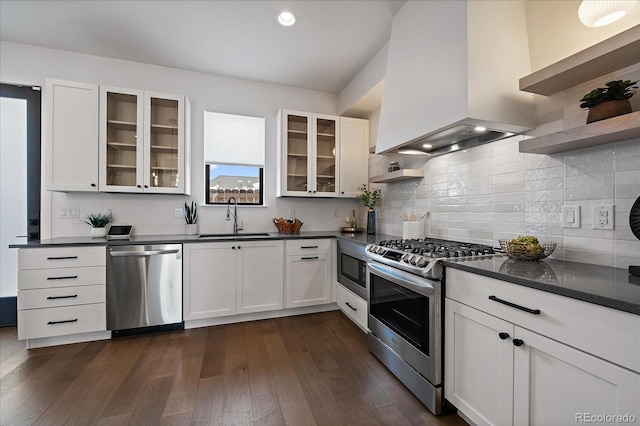 kitchen featuring a sink, stainless steel appliances, dark countertops, and wall chimney range hood