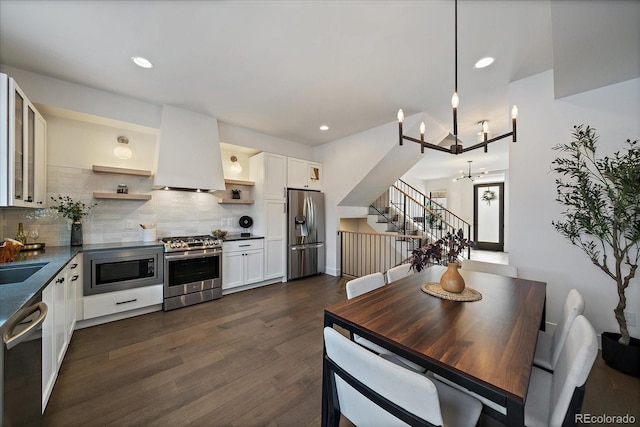 kitchen with a notable chandelier, open shelves, dark countertops, ventilation hood, and stainless steel appliances