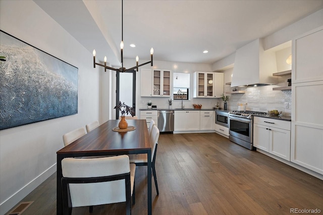 kitchen with visible vents, a sink, stainless steel appliances, dark countertops, and wall chimney exhaust hood