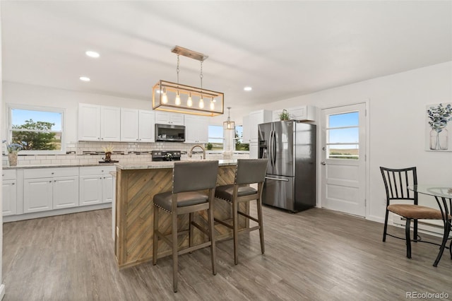 14475 Lanewood St, Brighton, CO 80603 - kitchen with stainless steel appliances, tasteful backsplash, white cabinetry, light wood finished floors, and a center island with sink