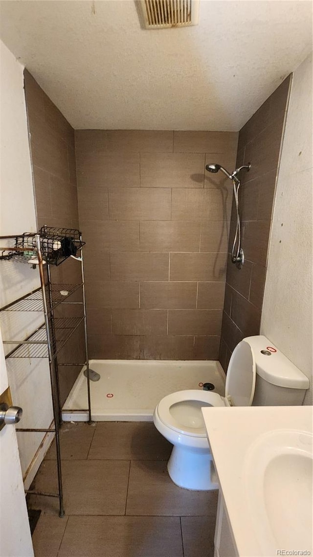 bathroom with a tile shower, a textured ceiling, tile patterned floors, vanity, and toilet