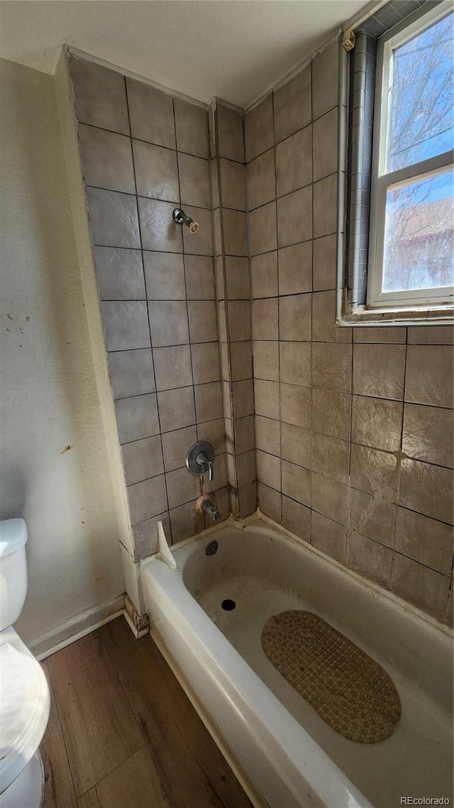 bathroom with wood-type flooring, tiled shower / bath, and toilet