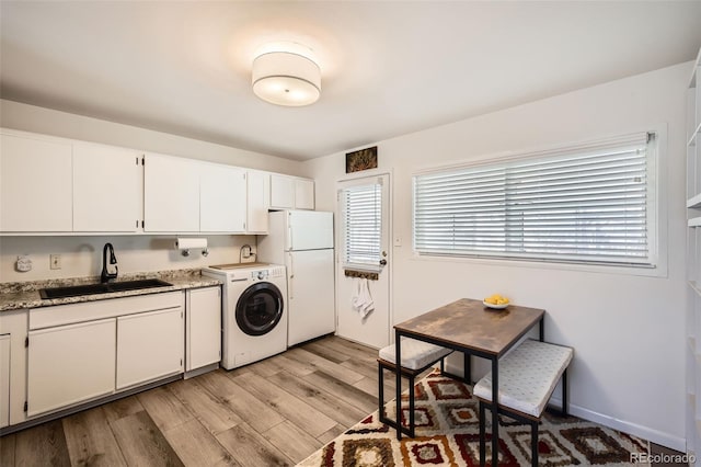 kitchen with light wood-style floors, freestanding refrigerator, white cabinetry, a sink, and washer / dryer