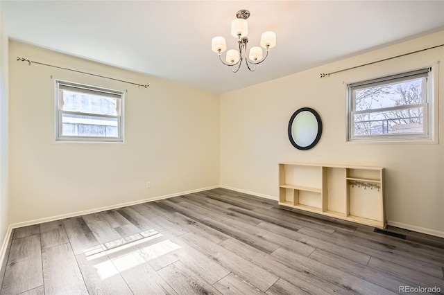 unfurnished dining area with a healthy amount of sunlight, an inviting chandelier, baseboards, and wood finished floors