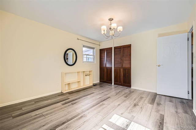 unfurnished bedroom featuring an inviting chandelier, baseboards, a closet, and wood finished floors