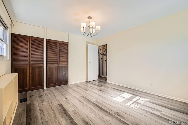 unfurnished bedroom with multiple closets, a notable chandelier, baseboards, and wood finished floors