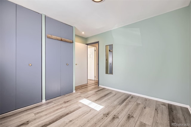 unfurnished bedroom featuring light wood-style floors, baseboards, and a closet