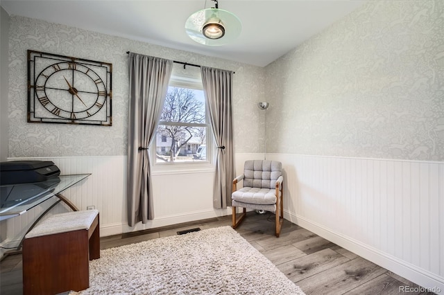 living area featuring a wainscoted wall, wood finished floors, visible vents, and wallpapered walls