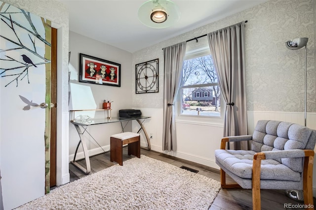 living area featuring wood finished floors, visible vents, baseboards, wainscoting, and wallpapered walls