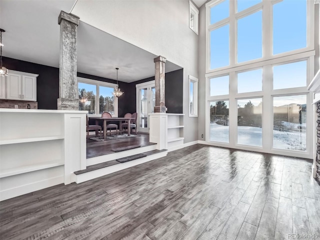 unfurnished living room featuring ornate columns, a towering ceiling, a chandelier, and hardwood / wood-style flooring