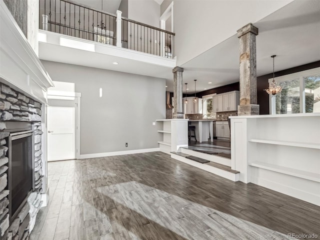 unfurnished living room with a chandelier, wood-type flooring, decorative columns, and a high ceiling