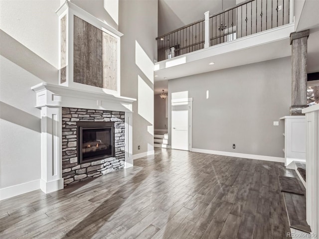 unfurnished living room featuring hardwood / wood-style flooring, a stone fireplace, and a high ceiling