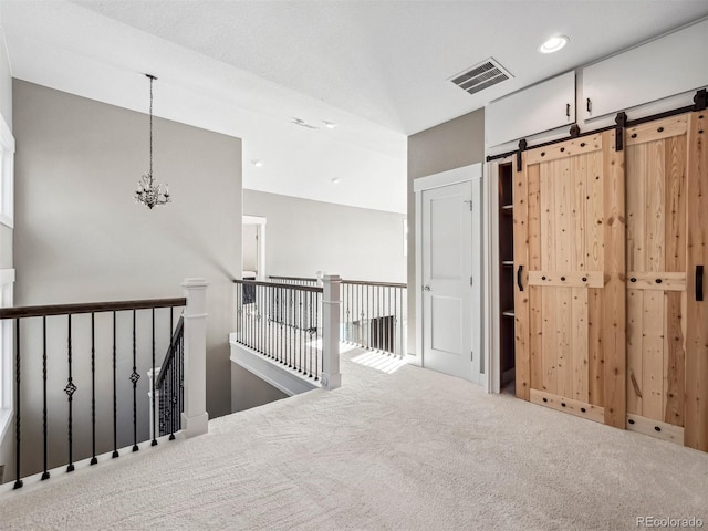 corridor with carpet flooring, a barn door, and a notable chandelier