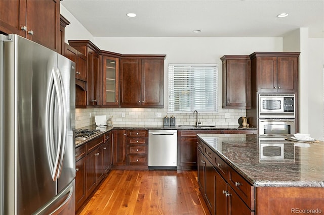 10368 Bluffmont Dr, Lone Tree, CO 80124 - kitchen with appliances with stainless steel finishes, wood finished floors, dark stone countertops, decorative backsplash, and recessed lighting