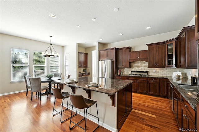10368 Bluffmont Dr, Lone Tree, CO 80124 - kitchen featuring appliances with stainless steel finishes, decorative backsplash, a chandelier, a center island, and wood finished floors