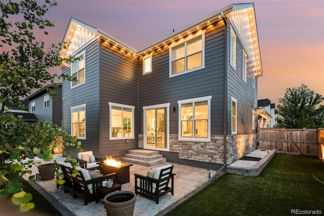 11187 W 53rd Dr, Wheat Ridge, CO 80033 - back of property at dusk featuring a patio area, stone siding, an outdoor living space with a fire pit, and a fenced backyard