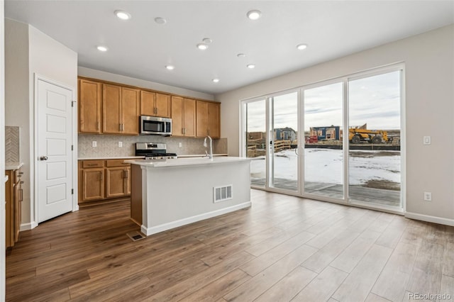 kitchen with hardwood / wood-style floors, decorative backsplash, a center island with sink, and appliances with stainless steel finishes