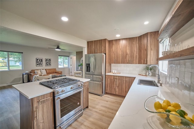 kitchen featuring decorative backsplash, premium appliances, light hardwood / wood-style flooring, ceiling fan, and sink