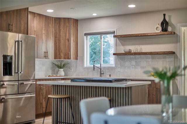 kitchen with high quality fridge, decorative backsplash, light wood-type flooring, and sink