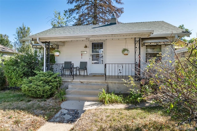 bungalow featuring covered porch, a chimney, and roof with shingles